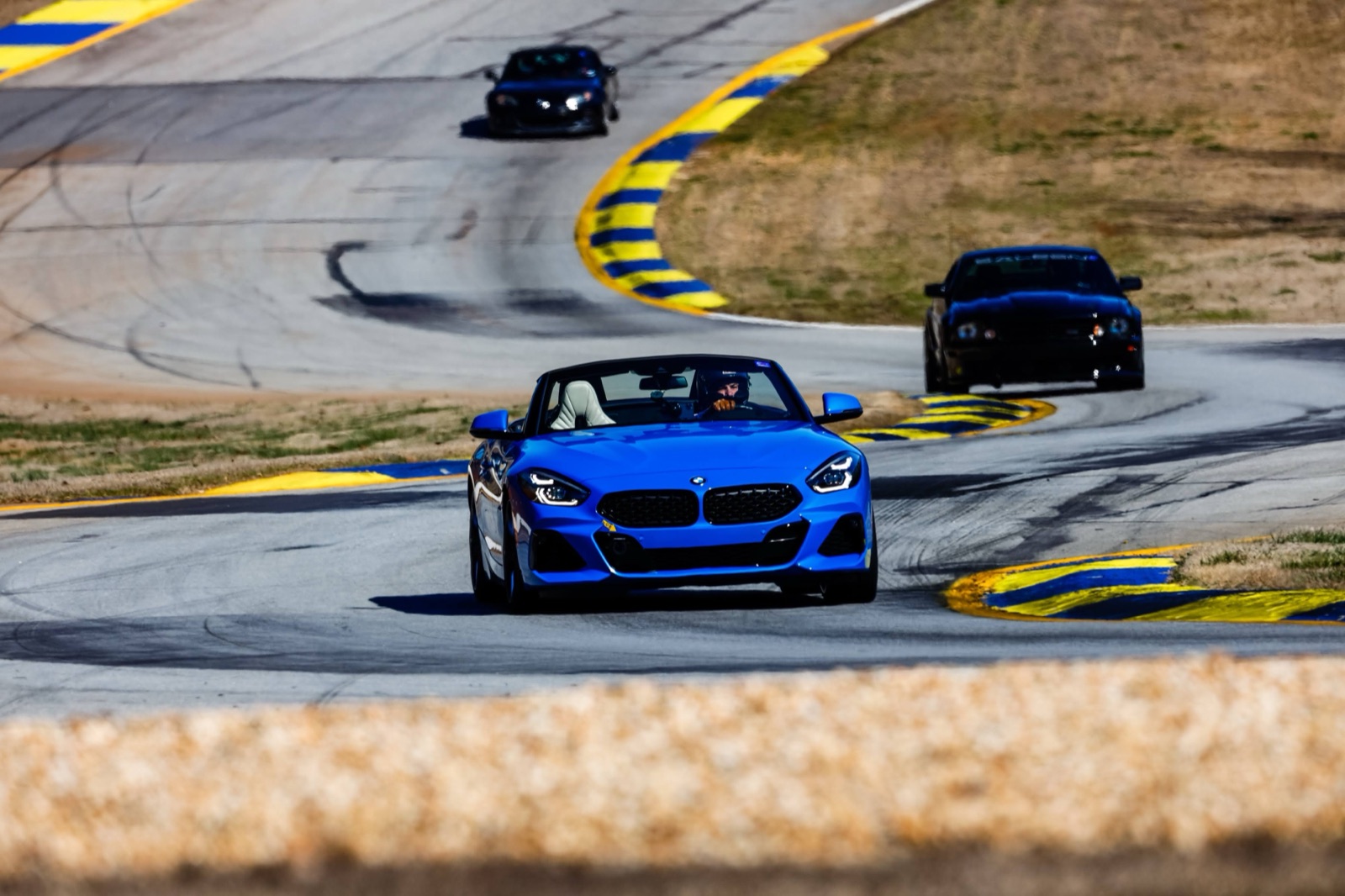 A blue BMW Z4 mid-corner at Road Atlanta with two more cars trailing through the same sweep.